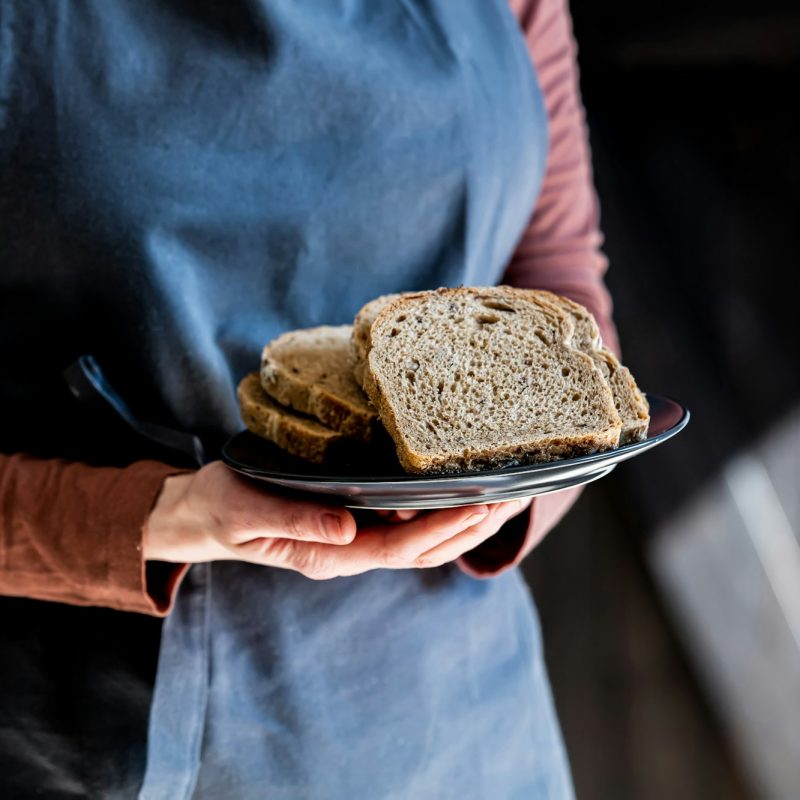 Female in apron holds plate with cut bread